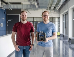 Moritz Schloegel (links) und Johannes Willbold analysierten die Sicherheit von Satelliten. In den Händen halten sie ein Modell eines Kleinsatelliten.(Bild: RUB, Marquard)