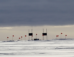 Die erste Station des Radio-Neutrino-Observatoriums auf dem grönländischen Eis. Die roten Fahnen markieren unterirdische Antennen, die von Solarmodulen (dunkle Rechtecke) mit Strom versorgt werden. (Bild: RNO-G, Cosmin Deaconu)
