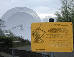 Der Zeitreiseweg am Radioteleskop Effelsberg beginnt am Besucherpavillon. Das Bild zeigt Station Nr. 1 (Einweihung und erste Messung 1971) vor dem Eingang des Pavillons und im Hintergrund das 100-m-Radioteleskop. (Bild: Norbert Junkes/MPIfR)
