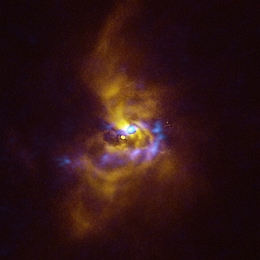 In der Mitte dieses Bildes ist der junge Stern V960 Mon zu sehen, der sich in über 5000 Lichtjahren Entfernung im Sternbild Monoceros befindet. Der Stern ist von staubigem Material umgeben, das das Potenzial zur Bildung von Planeten hat. Beobachtungen mit dem Instrument SPHERE (Spectro-Polarimetric High-contrast Exoplanet REsearch) am VLT der ESO, die in diesem Bild gelb dargestellt sind, zeigen staubiges Material, das den jungen Stern umkreist. Es sammelt sich in einer Reihe von verschlungenen Spiralarmen, die sich über Entfernungen erstrecken, die größer sind als das gesamte Sonnensystem. Die blauen Regionen zeigen Daten, die mit dem Atacama Large Millimeter/submillimeter Array (ALMA) gewonnen wurden, an dem die ESO beteiligt ist. Die ALMA-Daten geben einen tieferen Einblick in die Struktur der Spiralarme und offenbaren große Staubklumpen, die sich durch einen als „Gravitationsinstabilität“ bekannten Prozess zusammenziehen und kollabieren könnten, um Riesenplaneten von etwa der Größe des Jupiters zu bilden. (Bild: ESO/ALMA (ESO/NAOJ/NRAO)/Weber et al.)