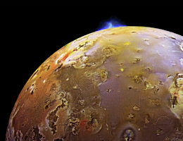 Ein halber Mond Io mit gelber Oberfläche, pockennarbigen grauen und bläulichen Bereichen. Gegen den schwarzen Weltraum zeichnet sich eine helle Eruptionswolke ab, die nach oben aufsteigt. Die meisten Berge auf Io sind Vulkane - und Eruptionen haben Raumsonden dort schon häufiger live beobachten können. Das Bild stammt von der NASA-Sonde Galileo. (Quelle: NASA/JPL/DLR).